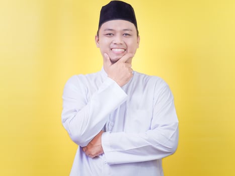 A smiling Asian Muslim man in white prayer clothes poses by holding his chin photo