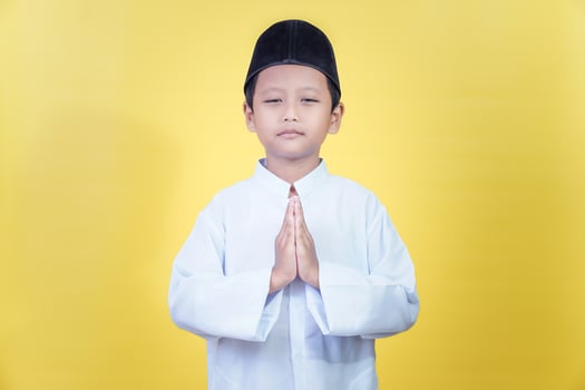 A young asian boy in traditional attire expresses joy and gratitude for Ramadan photo