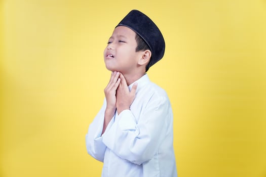 A boy in traditional Muslim dress looks thirsty while fasting against a bright yellow background. photo