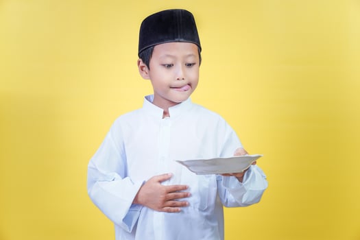 An asian boy in traditional Muslim dress eagerly holds a plate, ready to eat together. photo