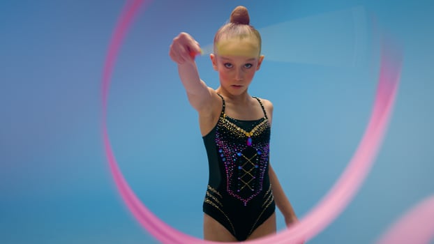 Serious Caucasian little kid child girl daughter schoolgirl student female gymnast dancer ballerina athlete in studio blue background twirling spinning gymnastic tape artistic element sport gymnastics photo