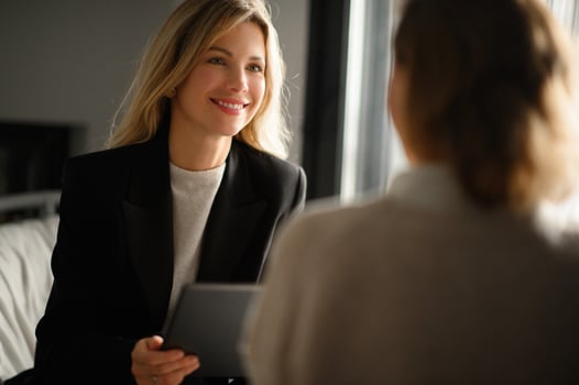 Two confident women in business attire having a discussion at a meeting table. Laptops, notebooks, and a cup of coffee are present as they brainstorm ideas photo