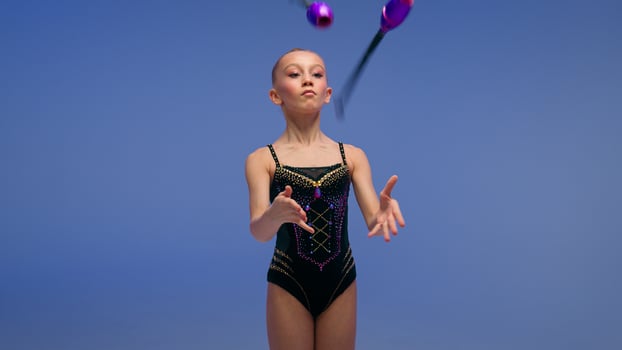Little kid gymnast girl child daughter dancer schoolgirl female acrobat ballerina young teen athlete juggler show sport exercise gymnastics competition twirling spinning juggling clubs blue background photo