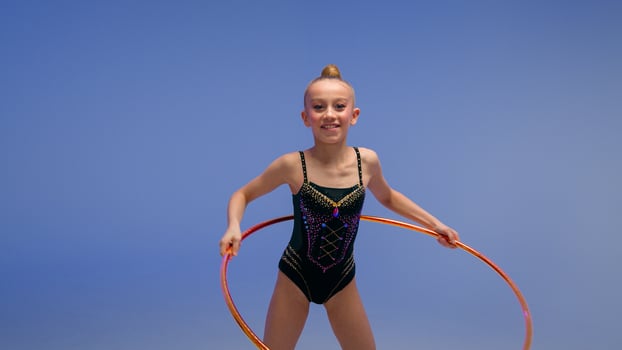 Caucasian little girl child kid daughter schoolgirl gymnast athlete dancer ballerina acrobat stand in split position flexibility artistic gymnastics spinning hoop sport event studio blue background photo