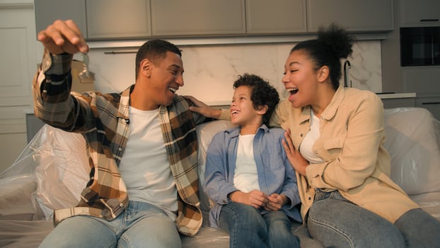 Happy African American family parents son on couch moving relocation day buy apartment rent house joyful father holding keys of new home mother child little boy kid rejoice loan mortgage bank credit photo