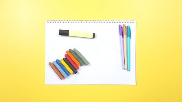 Various Color of Pens and Crayons with Highlighter and Notebook on Yellow Background photo