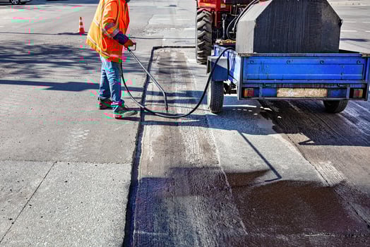 Road worker applying sealant on freshly paved street at mid-morning in an urban area photo