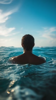 A man is floating in the ocean with his back to the camera photo