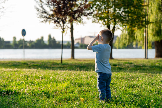 A little toddler boy of three and a half years old is standing in a summer park near a lake with his eyes closed. Childhood and nature. photo