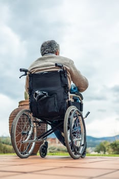 vertical Elderly man sitting on wheelchair looking at horizon in cloudy day photo