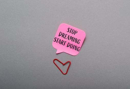 A pink note with the words Stop dreaming start doing written on it photo