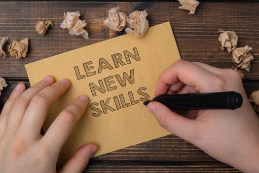 A person is writing on a piece of paper that says learn new skills photo