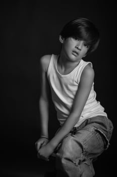 The boy, dressed in a white tank top and denim jeans, stands against a black background, his posture relaxed yet strong. photo