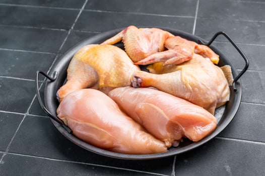 A black metal dish with a handle holds several pieces of fresh, raw chicken. The chicken is arranged neatly in the dish, and the background is a dark, tiled surface. photo