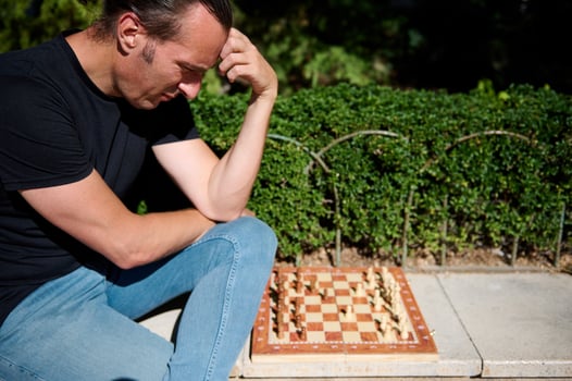 Man thinking deeply while playing an outdoor chess game on a sunny day photo
