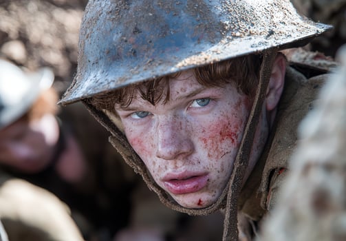 Close up of a young soldiers face, covered in dirt and blood, peering from a trench photo