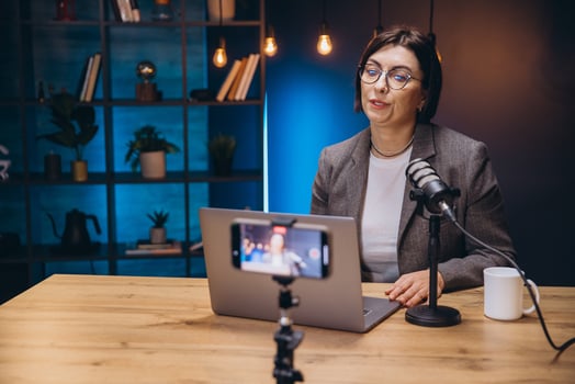 Female content creator recording podcast interview using professional microphone and smartphone at home workspace photo
