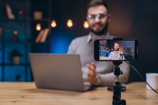 Influencer recording podcast in home studio using smartphone and microphone, laptop on desk photo