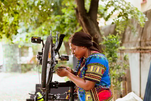 Determined female cyclist expertly using specialized equipment to adjust bike components in home yard. Sporty african American woman repairing bicycle frame with expert tools. photo