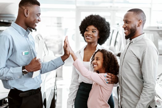 Lovely black girl high fiving friendly salesman at auto dealership. Positive African American family buying new car, making deal with manager at automobile showroom photo