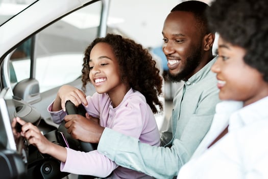 Cheerful black family checking car salon before buying new automobile, sitting inside auto, going on test drive. Positive Afro parents with daughter selecting vehicle at dealership photo