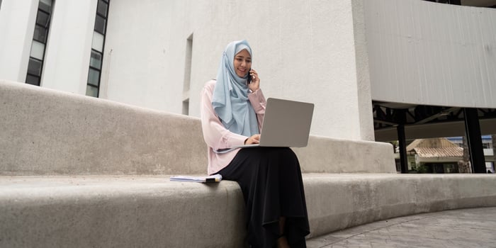 Muslim business woman in hijab talking on phone while working on laptop outdoors. photo