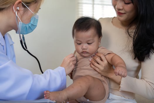 Pediatrician using stethoscope on baby held by mother during check-up. photo