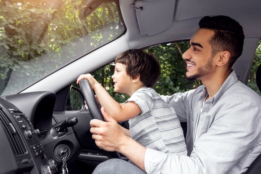 Smiling young man teaching little child to drive car in summer, boy hold steering wheel and look at road, profile, outdoor, copy space. Dad and son enjoy time together at weekend and driving lesson photo