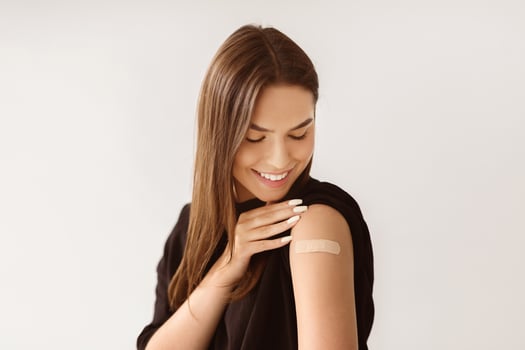 Prevention and treatment of flu. Caucasian woman patient showing shoulder with band aid after antiviral vaccine injection on light background. Immunization photo