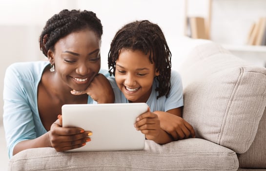 African Mom And Daughter Watching Cartoons Together On Digital Tablet, Lying On Couch. Free space photo