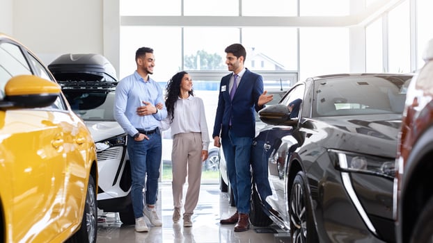 Handsome arab guy sales assistant giding young family husband and wife by newest car salon, cheerful salesman showing appropriate black auto for happy middle-eastern couple, full length shot photo