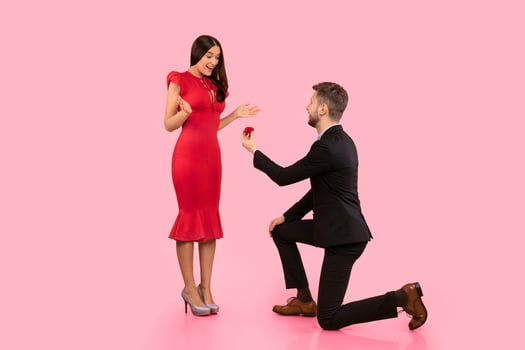 Marry Me. Boyfriend Proposing Standing On Knee Giving Engagement Ring To Girlfriend On Yellow Background. Studio Shot photo