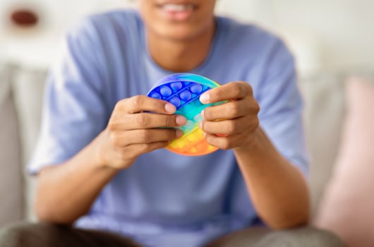 Closeup view of African American teenager playing with antistress POP IT toy at home. Unrecognizable black youth using sensory plaything to relieve stress or relax indoors photo