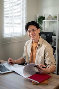 Smiling, satisfied Asian businessman is sitting at his desk in his office and smiling at the camera. photo
