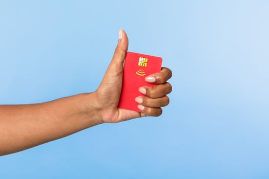 Cropped view of African American woman holding red credit card and showing thumb up gesture on blue studio background. Satisfied bank client recommending financial services, closeup photo