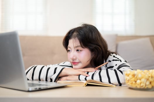 A tired Asian female student is resting her chin on her hands in front of her laptop while studying. photo