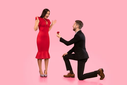 Proposal. Loving Man Offering Surprised Girlfriend Engagement Ring Standing On One Knee Over Yellow Studio Background photo