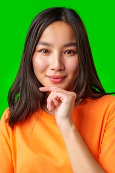 Young woman with long dark hair smiles while thoughtfully resting her chin on her hand in front of a vibrant green background photo