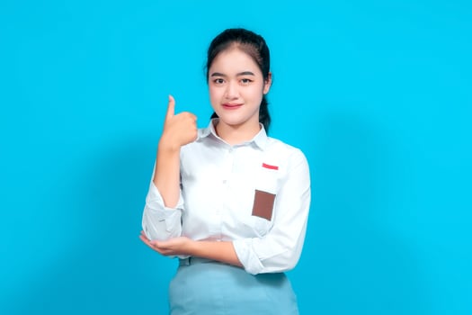 Young female student dressed in a uniform confidently gestures thumbs-up, standing against a blue background photo