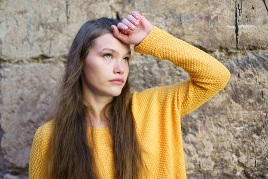 A young woman in a yellow sweater stands thoughtfully by a stone wall, exuding calm elegance photo