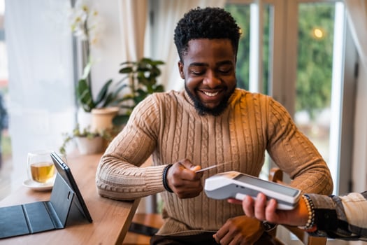 Young man in casual clothing makes a contactless payment with payment card while sitting in the cozy city cafe. photo