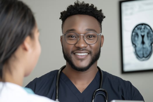 Smiling african adult doctor wearing glasses with stethoscope engaging with a patient in clinic with a brain scan visible in the background photo