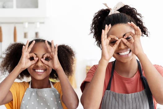 Happy black mother showing her teen daughter how to make cookies, cheerful african american mom and kid making dough for homemade pastry, fooling and smiling, kitchen interior, copy space photo