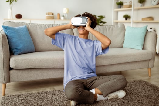 Full length of black teen guy wearing VR headset and enjoying cyberspace exploration at home. African American adolescent absorbed in virtual reality. Modern technologies in everyday life concept photo