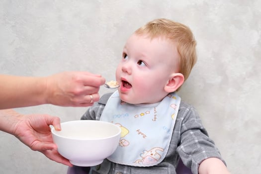 mother feeds little boy porridge from a spoon photo