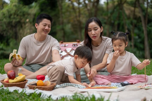 A cheerful Asian family enjoys a picnic in a green public park, sitting on a blanket, and eating. photo