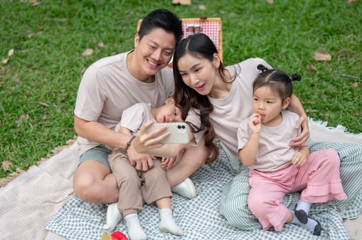 A cheerful Asian mom takes a selfie with her family during a weekend picnic in a park. photo