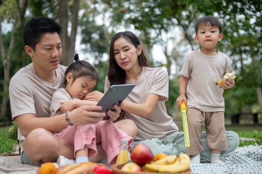 A happy Asian parents are taking their little kids on a picnic in a green park. photo