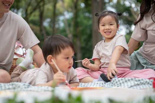 A cute little Asian girl enjoys coloring on a canvas while picnicking with her family in the park. photo