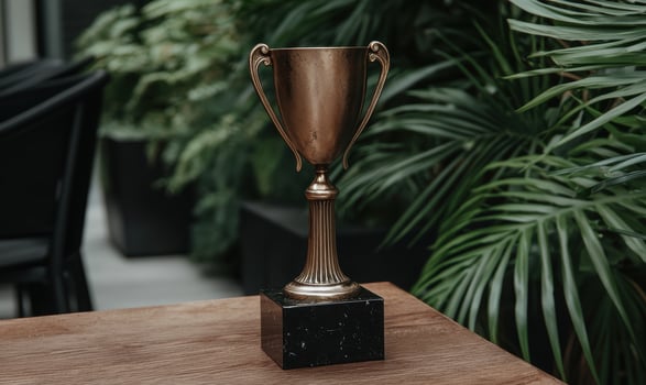 Bronze trophy on wooden table with green plants in background photo